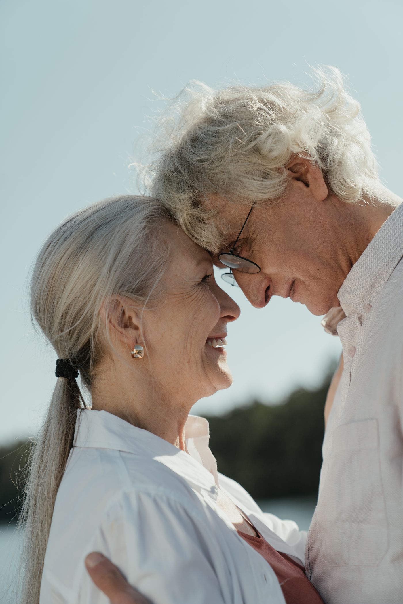 An older couple laughing together outdoors, foreheads touching